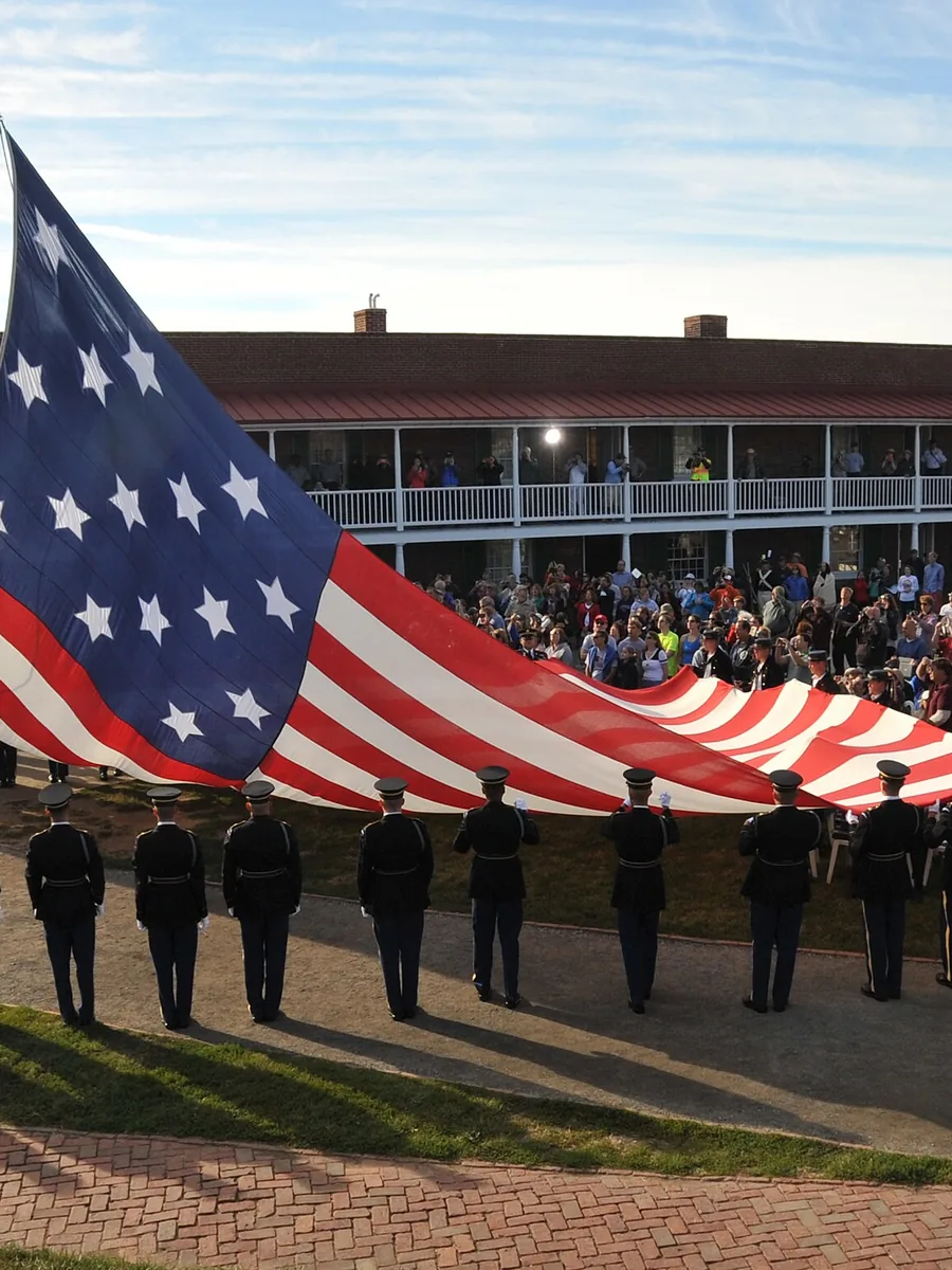 Coast Guard members holding a huge 15-star flag in front of the barracks at Fort McHenry