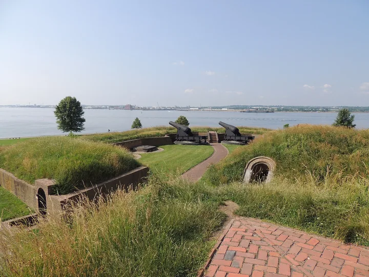A grass-covered bastion with black cannons on top, above the wide Patapsco River