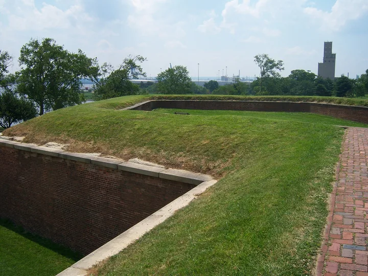 The grassy top of a brick bastion at Fort McHenry curving away toward the Baltimore skyline