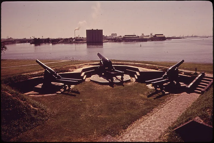 1970s photo of black cannons on the outer battery, with a cargo terminal across the water