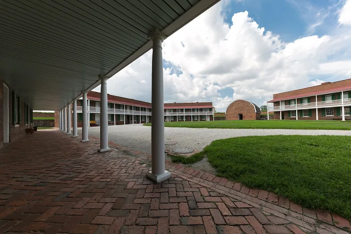 The covered brick porch of a barracks building looking out over the parade ground and the arched powder magazine