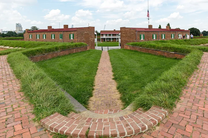 Brick paths crossing a green bastion lawn toward the barracks, with the flag beyond