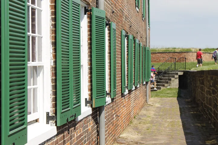 Green wooden shutters along a brick barracks wall, with a grassy rampart beyond