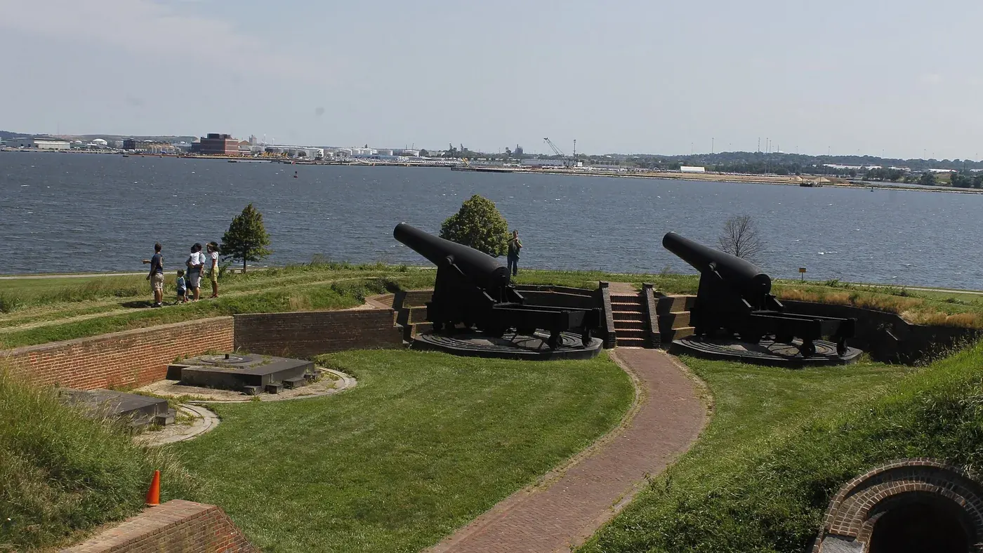 Black cannons on the outer battery facing the wide river, with a few visitors on the grass
