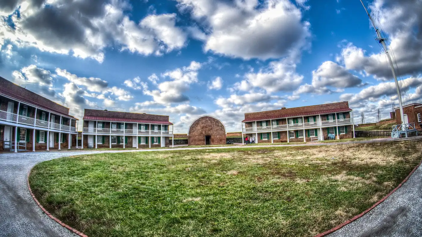 Wide fisheye view of the parade ground inside the star fort, ringed by brick barracks under a big cloudy sky