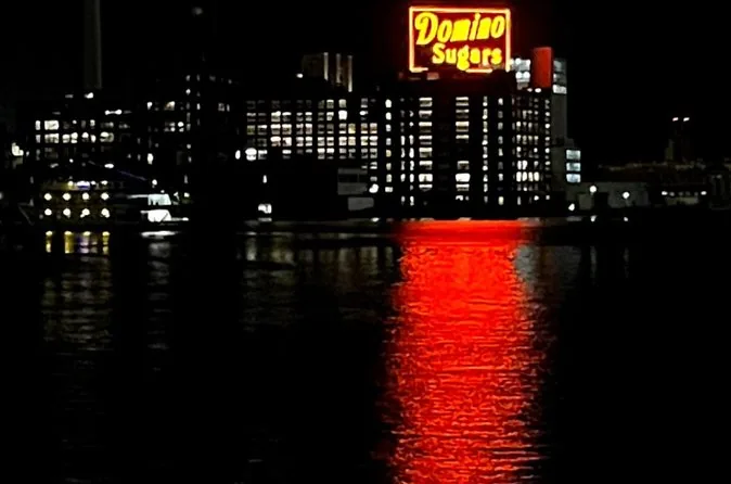 The red neon Domino Sugars sign glowing above the harbor at night, reflected in the water
