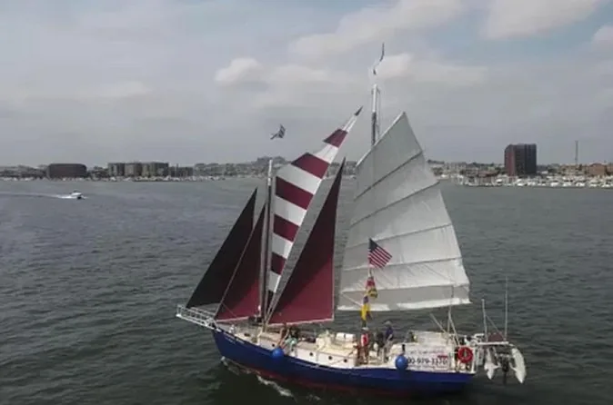 A schooner with red and white striped sails heading across the open harbor